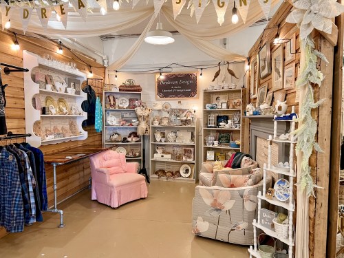 A cozy shop display featuring vintage decor, shelves of crafts, and seating areas with soft lighting and wooden accents.