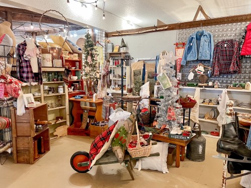 A cozy vintage shop filled with holiday decor, rustic furniture, and various charming items for sale.