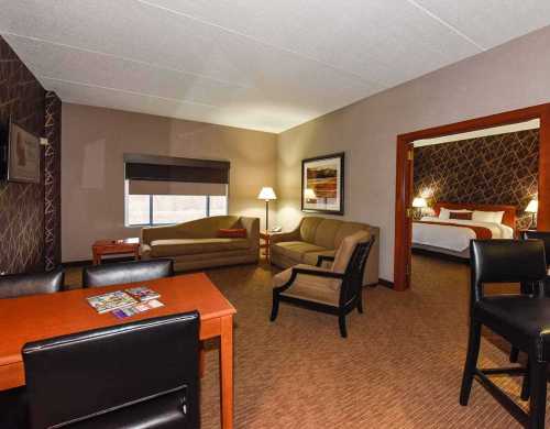 A cozy hotel room featuring a seating area, desk, and a separate bedroom with a large bed.