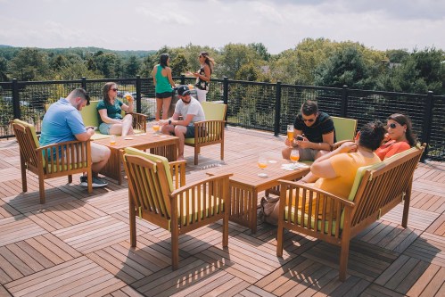 A group of people relax on a rooftop deck, enjoying drinks and conversation on a sunny day.