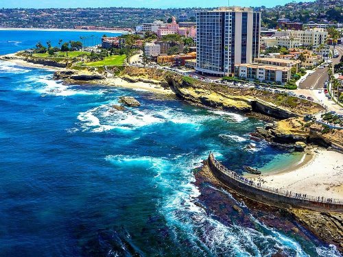 Aerial view of La Jolla coastline, featuring cliffs, ocean waves, and buildings along the shore.