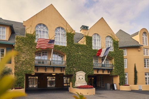 A charming hotel facade adorned with ivy, featuring American and French flags, and a welcoming entrance.