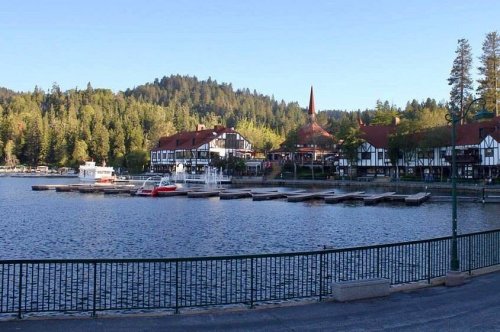 Scenic lakeside view with boats, wooden docks, and charming buildings surrounded by lush green trees and mountains.