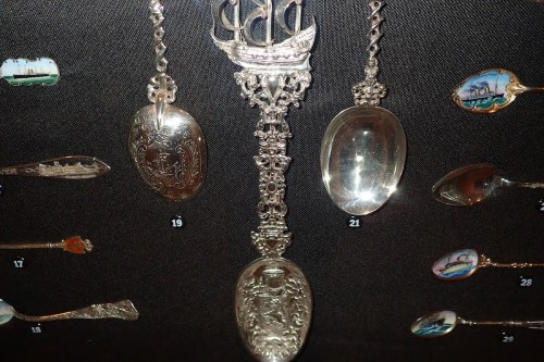 A display of ornate silver spoons and a ship-shaped handle, showcasing intricate designs and details.