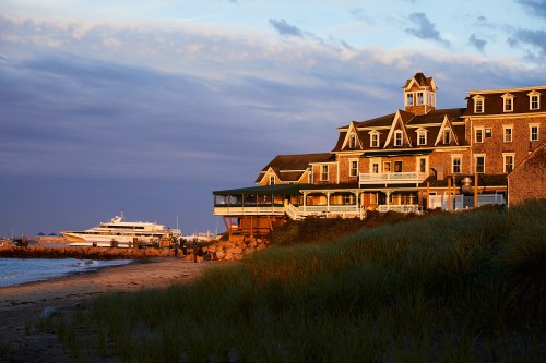 A seaside hotel at sunset, with a boat docked nearby and beach grass in the foreground.