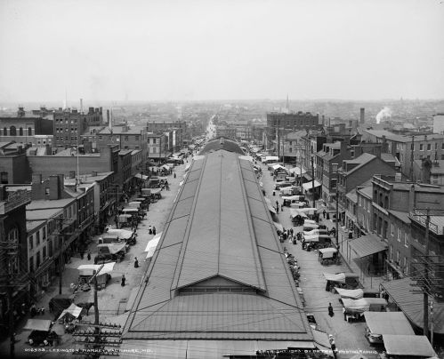 Aerial view of a bustling market street with tents and buildings, capturing a historic urban scene.