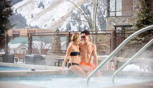 A couple relaxes in a hot tub surrounded by snowy mountains, enjoying each other's company.