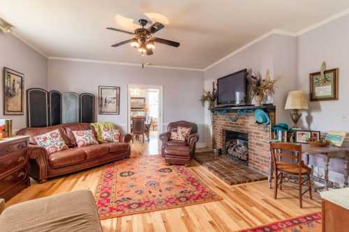 Cozy living room with a leather sofa, fireplace, wooden floor, and decorative rug, leading to a dining area.