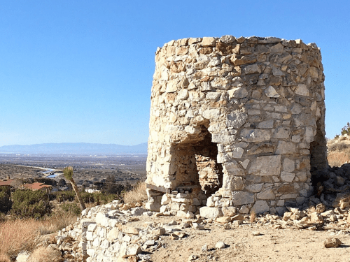 Stone structure on a hillside with a clear blue sky and distant mountains in the background.
