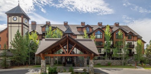 A large lodge-style building with a wooden entrance, surrounded by trees and a blue sky.