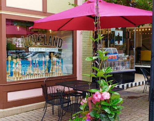 A pink umbrella shades a table outside Loveland Sweet Shoppe, featuring ice cream and candy in the window.