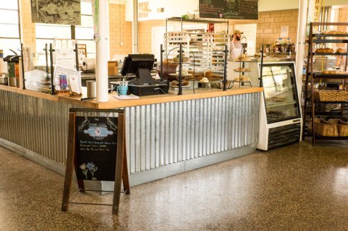A cozy café interior featuring a metal counter, display cases, and a chalkboard menu in a bright, inviting space.