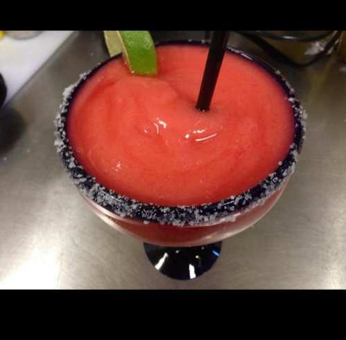 A vibrant frozen cocktail in a salt-rimmed glass, garnished with a lime wedge and a straw.