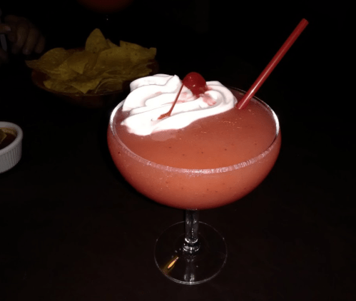 A vibrant strawberry cocktail topped with whipped cream and a cherry, served in a large glass with a red straw.