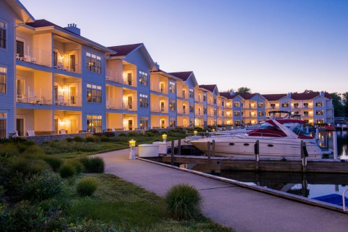 A serene waterfront scene at dusk, featuring illuminated apartment buildings and boats docked along a calm marina.