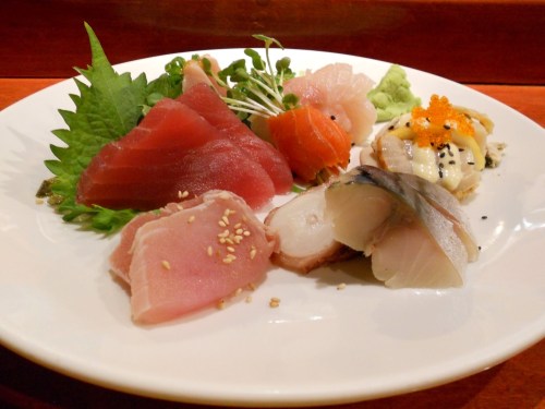 A plate of assorted sushi and sashimi, featuring various fish, garnished with greens and sesame seeds.