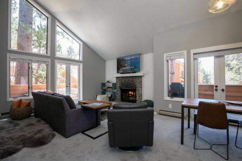 Cozy living room with a fireplace, large windows, and modern furniture, surrounded by trees.