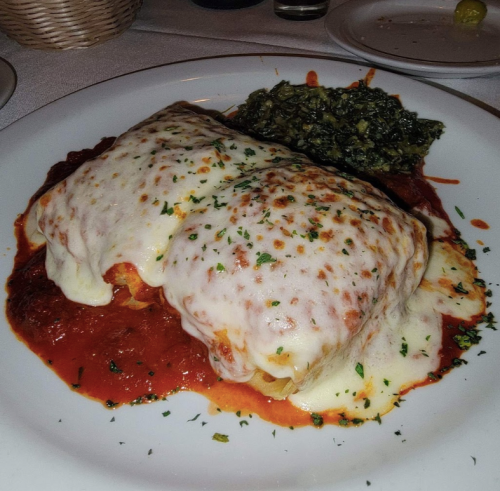 A plate of lasagna topped with melted cheese and marinara sauce, served with a side of sautéed greens.