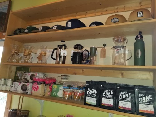 A wooden shelf displaying various coffee brewing equipment, hats, and packaged coffee products.