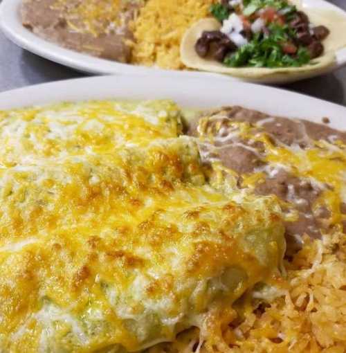 A plate of cheesy enchiladas with rice and refried beans, alongside a taco topped with lettuce and salsa.