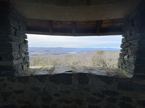 View from a stone window overlooking rolling hills and valleys under a clear sky.
