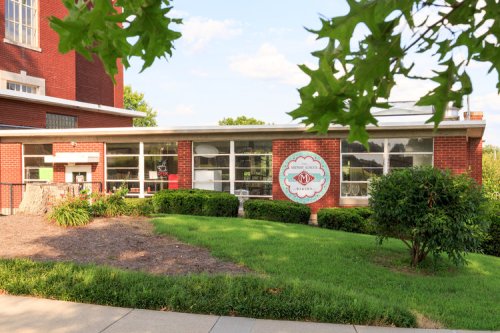 A brick building with large windows and a green lawn, featuring a sign that reads "Gallery" on the front.