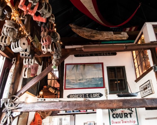 A rustic interior filled with nautical artifacts, including ropes, pulleys, and a painting of sailboats on the wall.