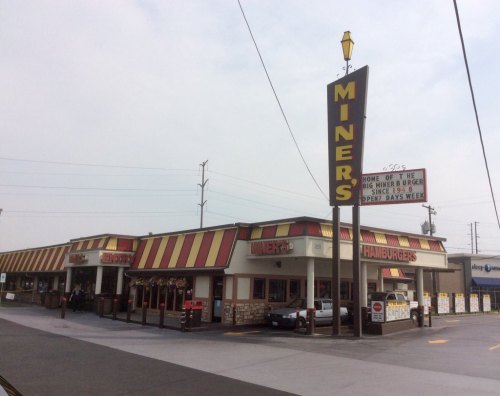 A retro-style hamburger restaurant with a large sign reading "Miners Hamburgers" and a drive-thru area.