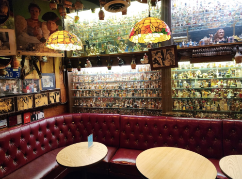 Cozy restaurant interior with red leather seating, wooden tables, and shelves filled with colorful collectibles.