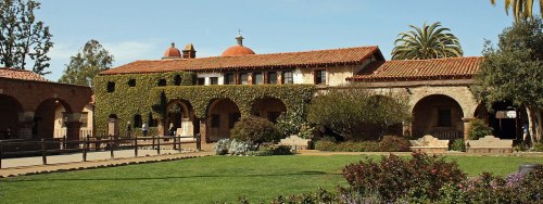Historic building with red-tiled roof, ivy-covered walls, and lush greenery in a sunny outdoor setting.