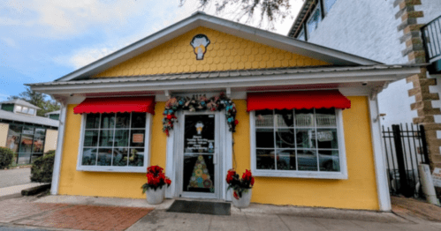 A bright yellow building with red awnings, decorated for the holidays, featuring a festive window display.