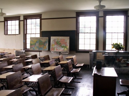 A vintage classroom with wooden desks, large windows, and maps on the wall, creating a nostalgic educational atmosphere.
