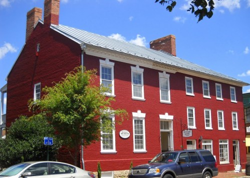 A red brick building with a metal roof, featuring multiple windows and a sign, set against a blue sky.