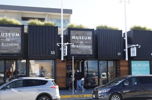 Exterior view of the Museum of Illusions, featuring shipping container architecture and greenery on the roof.