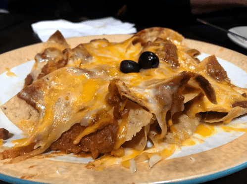 A plate of nachos topped with melted cheese, beans, and black olives.