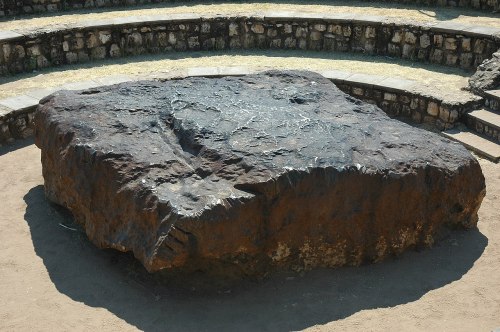 A large, flat rock sits in an outdoor amphitheater, surrounded by stone seating and grass.