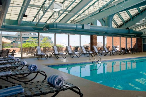 Indoor swimming pool with lounge chairs and rolled towels, surrounded by large windows letting in natural light.