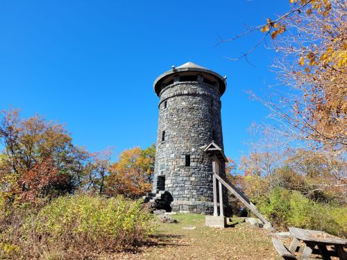 A stone tower surrounded by autumn foliage under a clear blue sky.