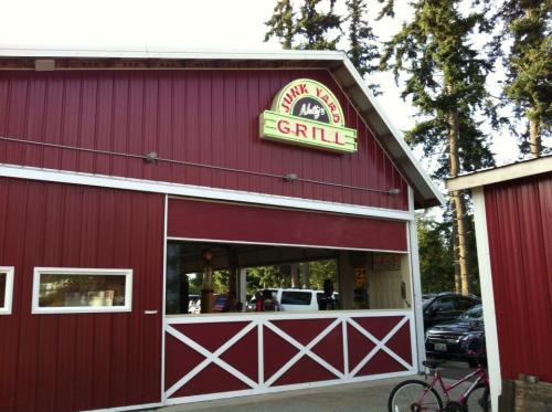 A red barn-style building with a sign reading "Junk Yard Grill" and a bike parked nearby. Trees in the background.