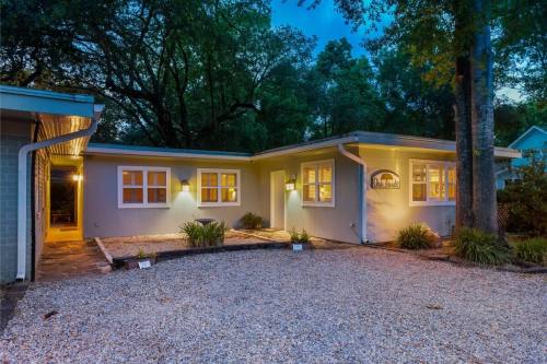 A modern home exterior at dusk, featuring a gravel driveway, illuminated windows, and surrounding greenery.