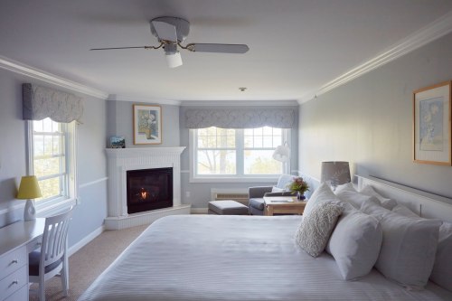 Bright, cozy hotel room with a king bed, fireplace, armchair, and large windows overlooking a scenic view.