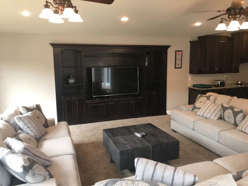 Cozy living room with a large TV, dark wood entertainment center, and light gray sofas arranged around a black coffee table.