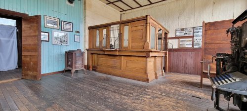 Interior of a historic room featuring wooden furniture, a counter with bars, and framed photos on the walls.