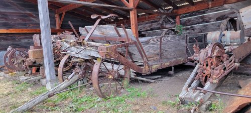 Old wooden farm equipment and machinery stored under a rustic shed, showcasing weathered wood and rusted metal parts.