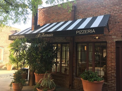 A brick building with a black and white striped awning reading "Il Formaio Pizzeria" and potted plants outside.