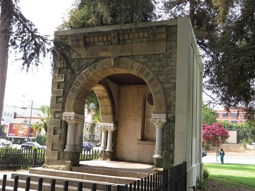 Historic stone structure with an arch, labeled "Public Library," surrounded by trees and a fence.