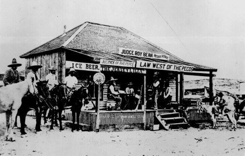 Historic black-and-white photo of a building labeled "Law West of the Pecos," with people and horses outside.