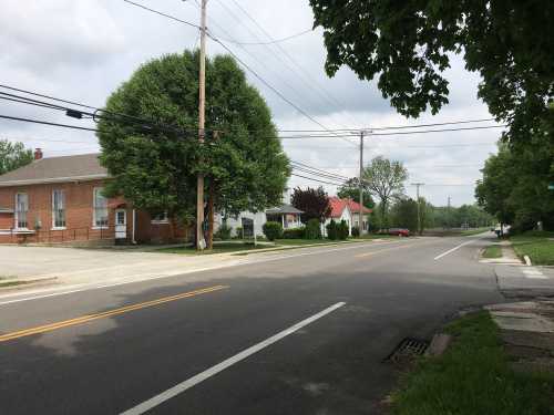 A quiet street scene with a tree, power lines, and a few buildings, under a cloudy sky.