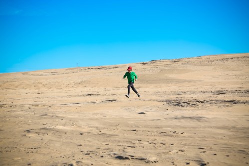 A person in a green shirt and red hat runs across a sandy desert landscape under a clear blue sky.