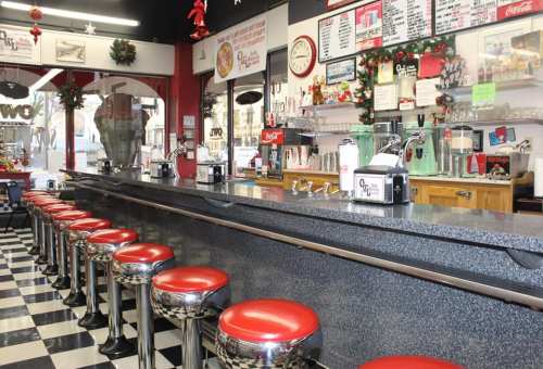 A retro diner interior featuring a long counter with red stools, checkered floor, and festive decorations.